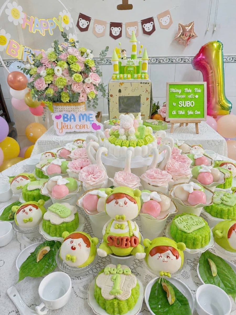 Mâm cúng thôi nôi tông xanh lá của Hảo Tâm An — rau câu lâu đài tạo hình, xôi, chè, bánh bao và hoa tươi bày trên chén dĩa sứ